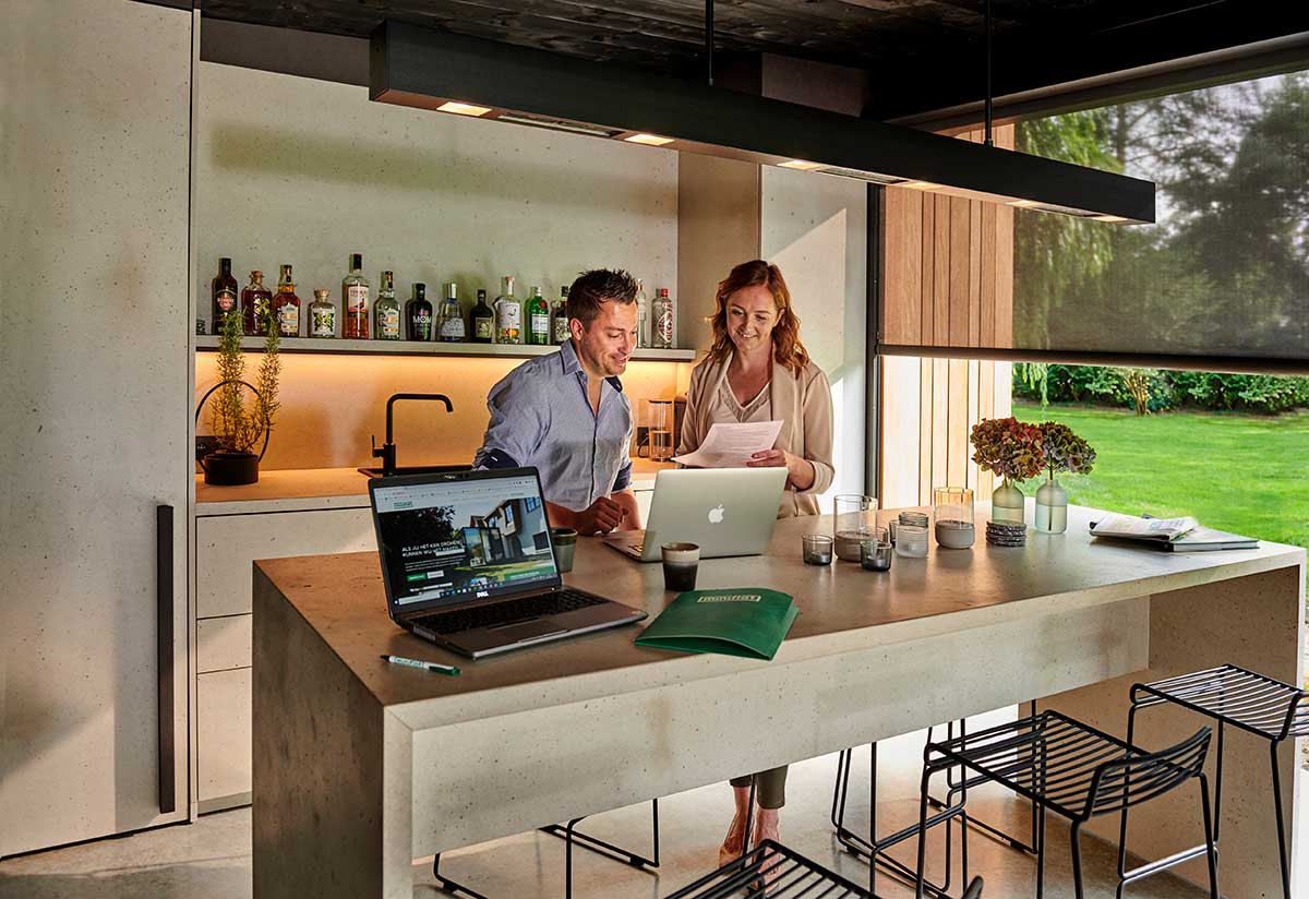  Ein Mann und eine Frau mittleren Alters arbeiten gemeinsam an Laptops in der modernen Küche eines Poolhauses in Mülheim. 