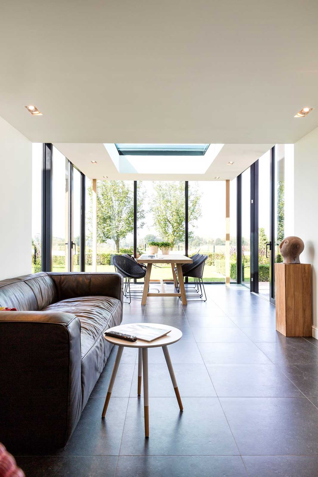  Heller, offener Wohn- und Essbereich in einem modernen Wintergarten in Mülheim mit Ledersofa und Blick in den Garten. 