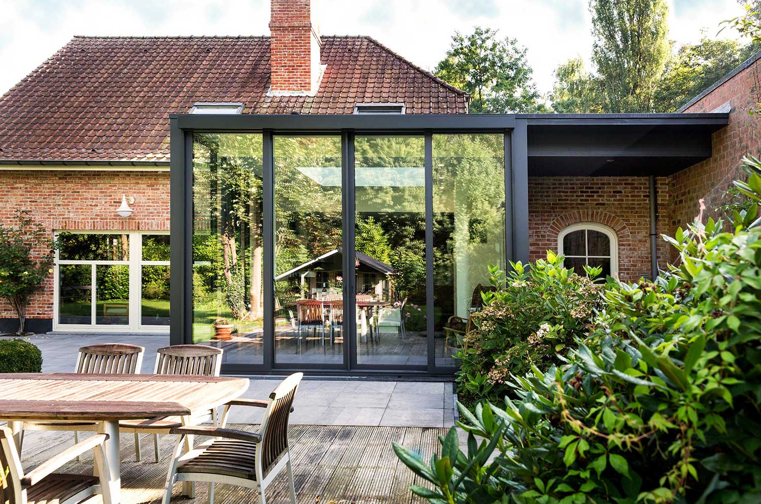  Moderner Wintergarten-Anbau in Mülheim mit großen Glasschiebetüren an einem Backsteinhaus mit Terrasse und Gartenmöbeln. 