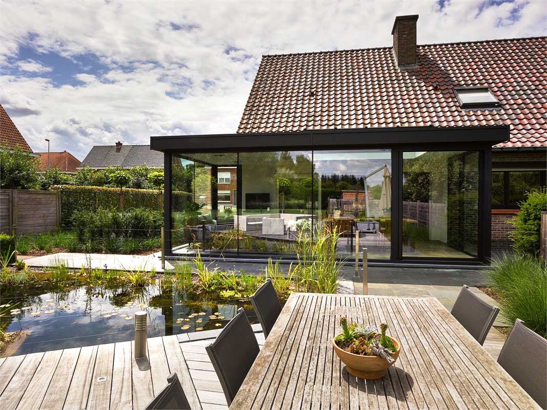  Aluminium Wintergarten in Mülheim mit großen Glasfronten, angrenzender Terrasse am Teich und Blick in den hellen Innenraum. 