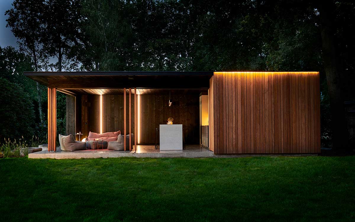  Beleuchtetes, modernes Poolhaus aus Holz in Mülheim bei Nacht mit Lounge-Bereich und stimmungsvoller Außenbeleuchtung im Garten. 