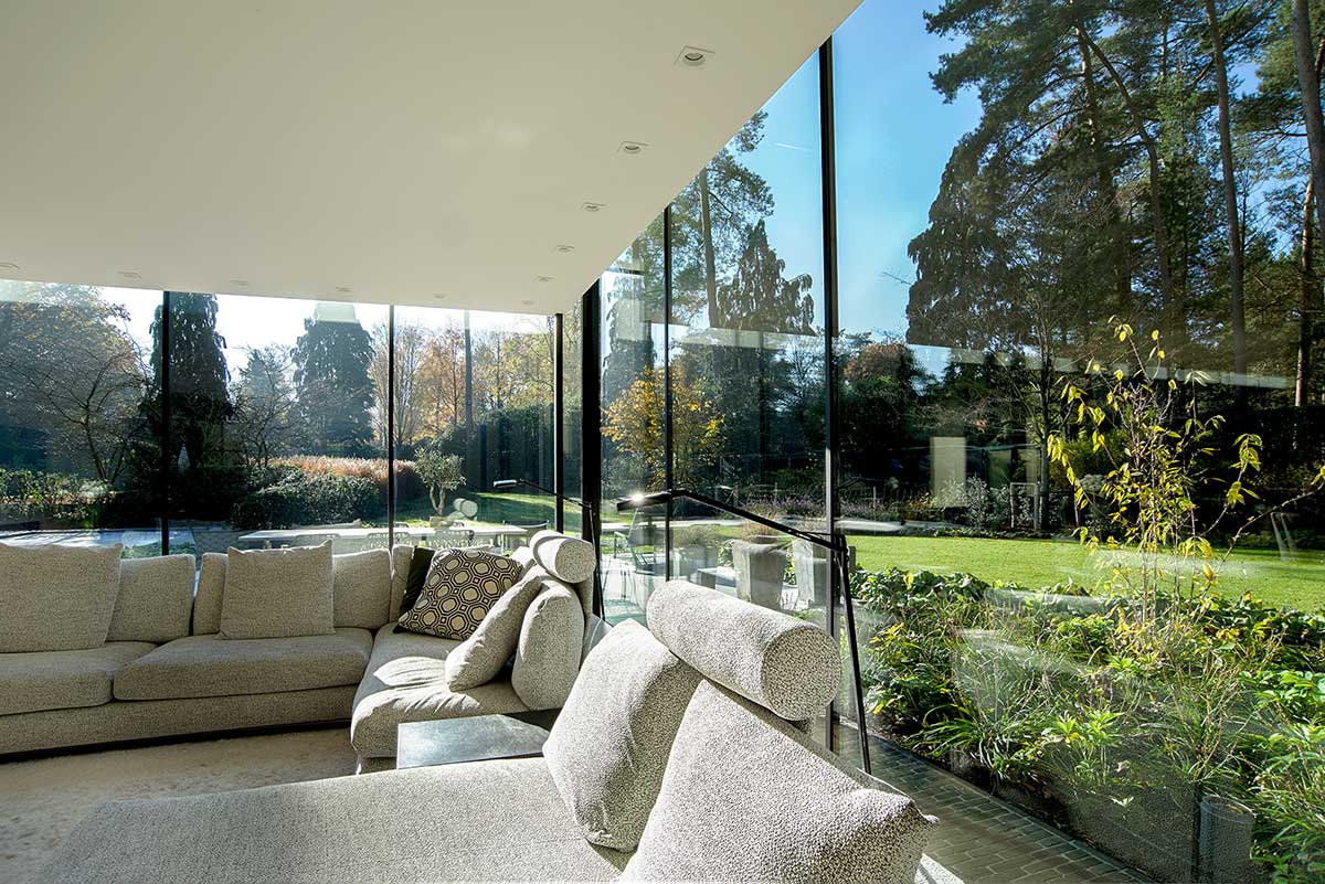  Moderner, lichtdurchfluteter Wintergarten-Wohnbereich in Mülheim mit beiger Eckcouch und Panoramablick durch große Fenster in den Garten. 