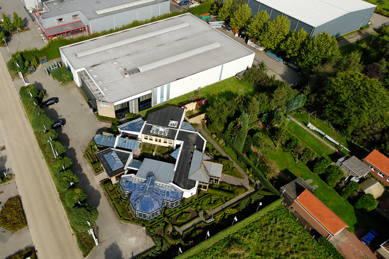 Luftaufnahme des modernen Wintergarten-Zentrums in Antwerpen mit verschiedenen Ausstellungsmodellen, umgeben von gepflegten Grünflächen und Parkplätzen.