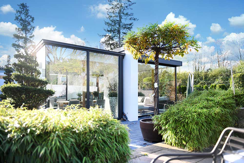 Moderner Glasanbau in Mülheim mit schwarzem Rahmen, umgeben von üppigem Grün und Bambus. Helle, offene Gestaltung.