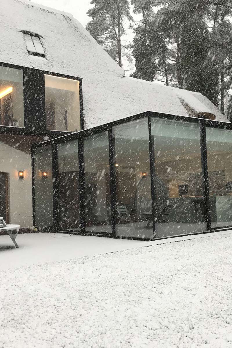 Winterlicher Glas-Wintergarten in Mülheim an einem reetgedeckten Haus während eines Schneefalls. Schnee bedeckt den Boden und die Umgebung.