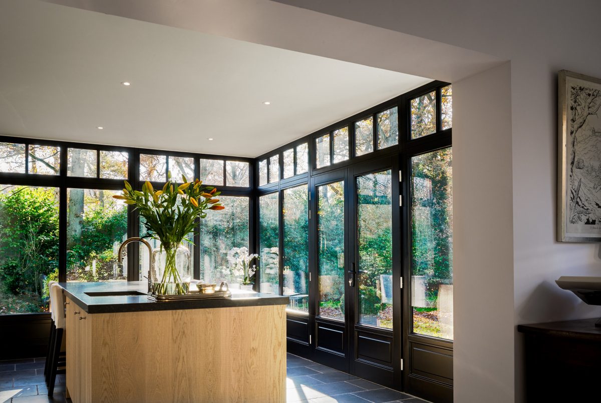 Helle, moderne Küche in Mülheim mit Kochinsel, großen Fensterfronten zum Garten und viel Tageslicht. Blumen in einer Vase auf der Arbeitsfläche.