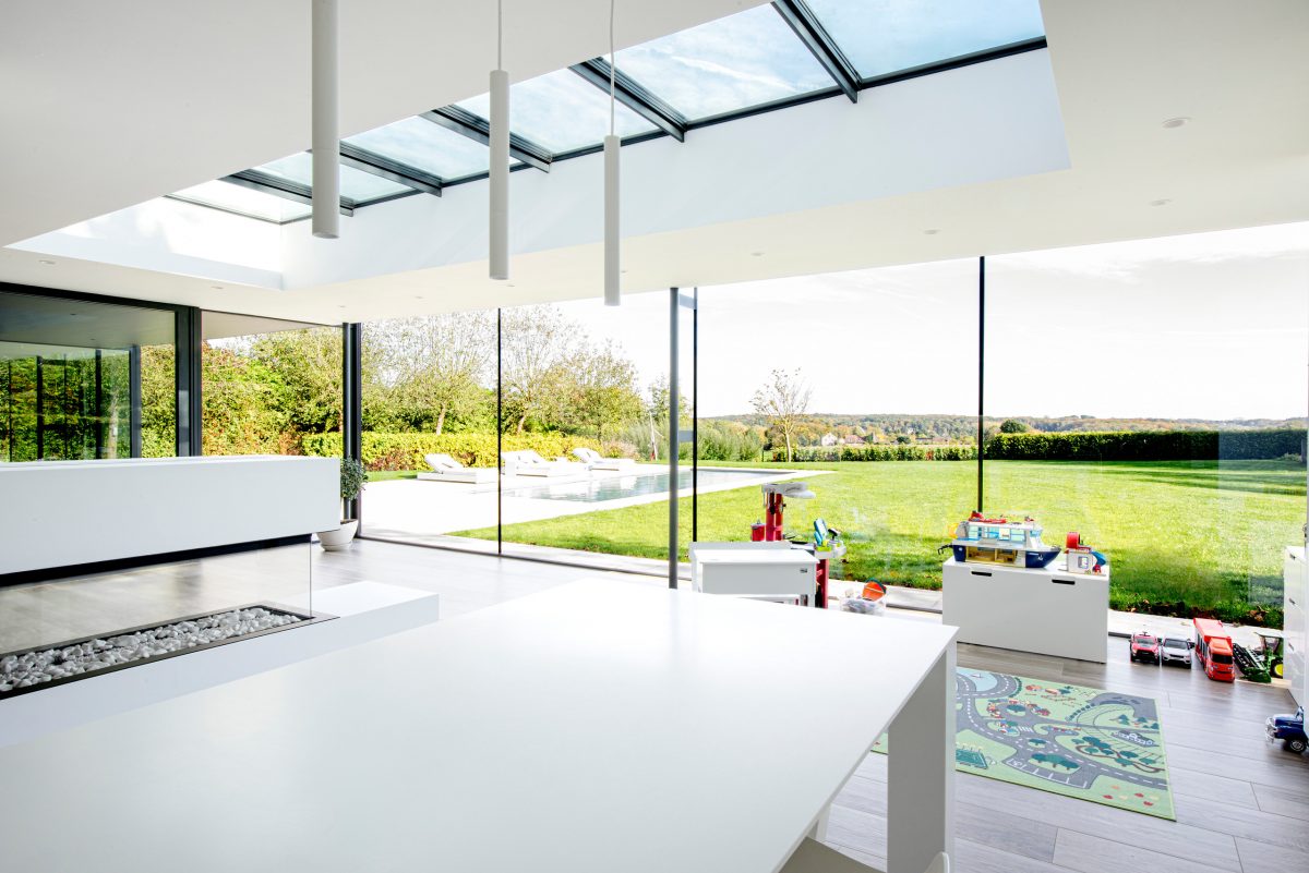 Heller, moderner Wohnbereich mit weißer Arbeitsplatte, Glaswänden, Oberlichtern und Blick auf einen Garten mit Pool.