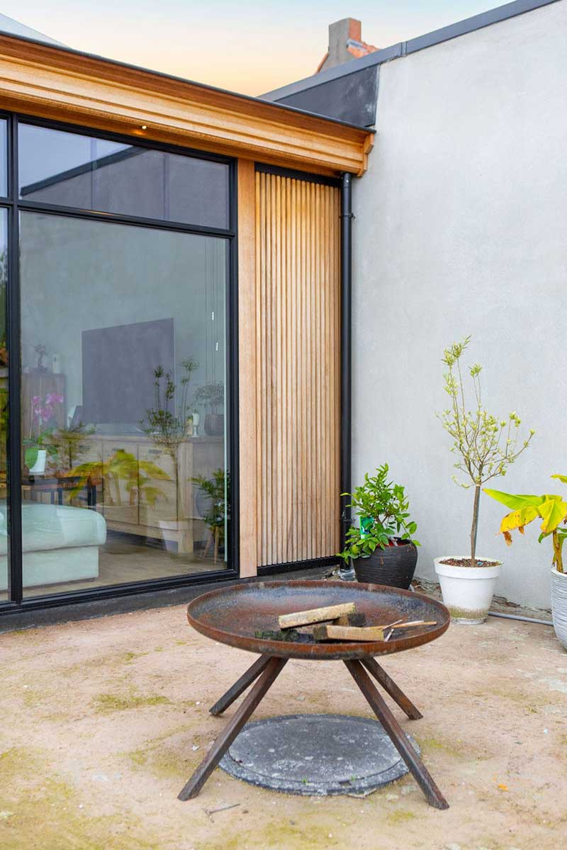 Moderner Glas-Wintergarten in Mülheim mit schwarzem Rahmen, angrenzender Terrasse mit Esstisch und Blick auf einen grünen Garten mit Pool.