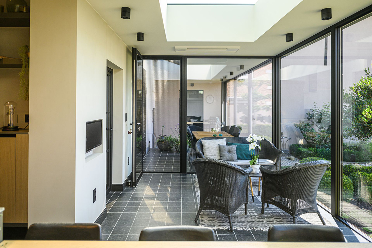 Heller, moderner Wohnbereich in Mülheim mit Glaswänden, Oberlichtern, grauen Fliesenboden, Korbsesseln und Blick in den begrünten Außenbereich.