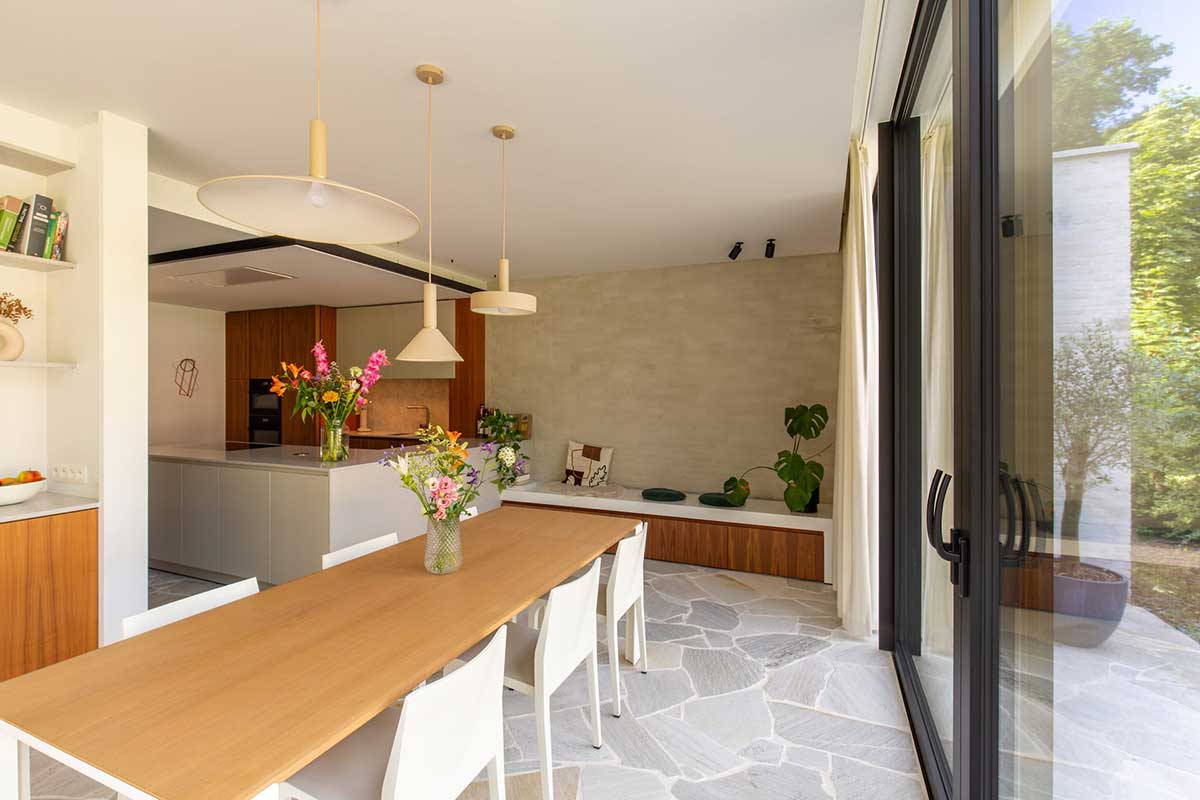 Heller, offener Wohnbereich in Mülheim mit Holztisch, weißen Stühlen, moderner Küche im Hintergrund und großen Schiebetüren zum Garten.