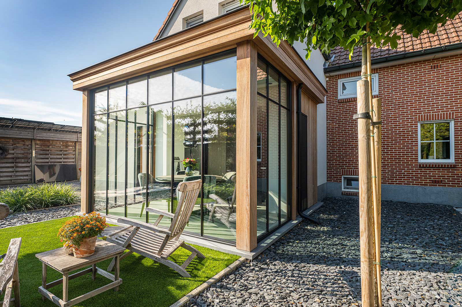 Geräumige, moderne Stahl-Holz-Veranda mit Glasfront und gemütlicher Sitzecke im Garten.