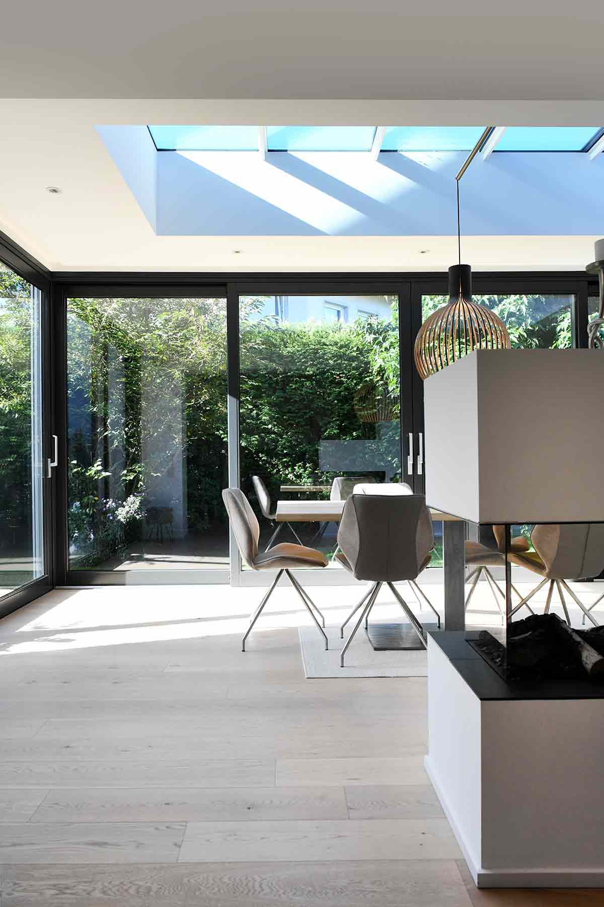 Lichterfüllter Wintergarten in Mülheim mit Esstisch, modernen Stühlen, Designleuchte, Kamin und großem Oberlicht.