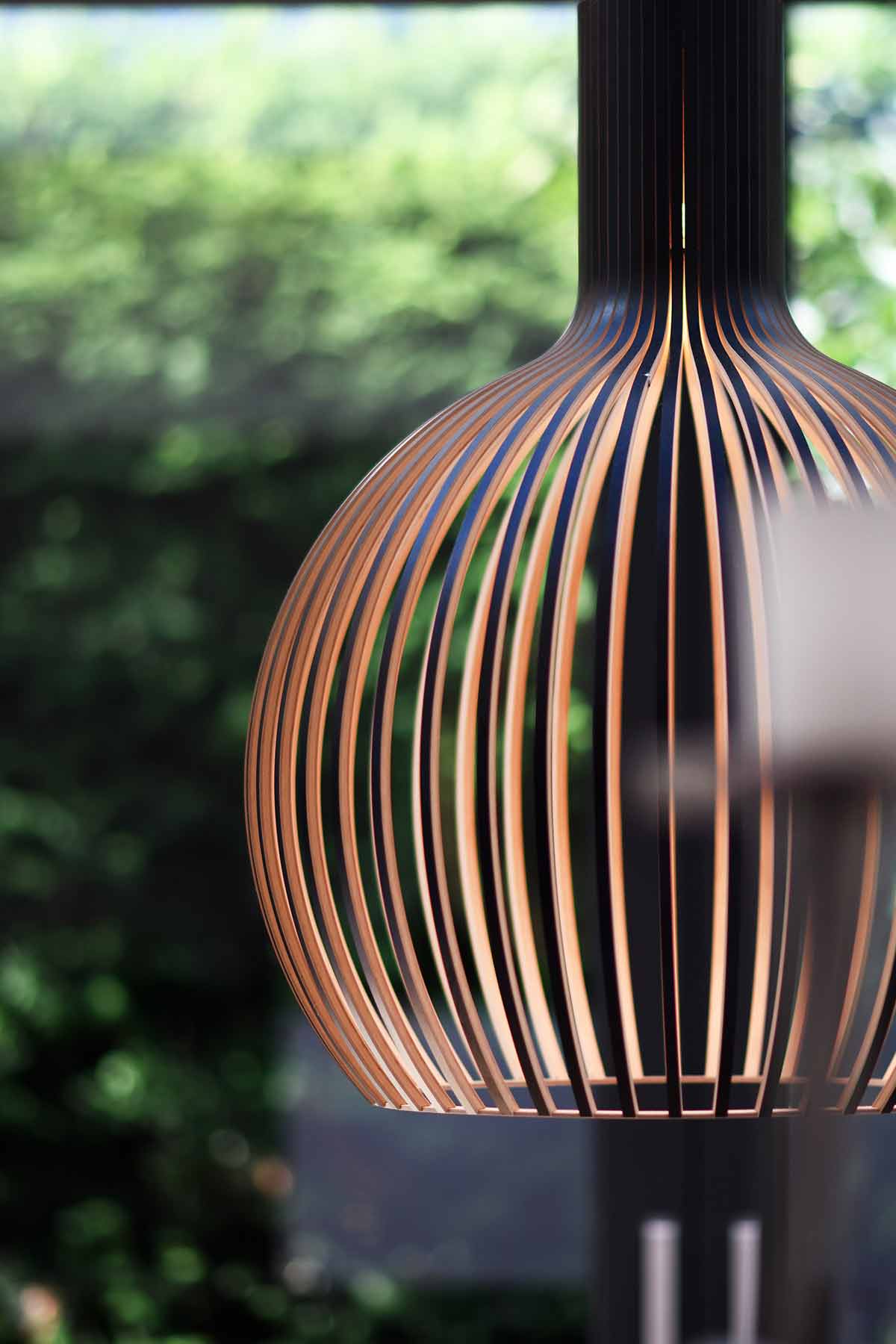 Nahaufnahme einer Secto Design Octo 4240 Pendelleuchte aus Birkenholz vor verschwommenem Grün.